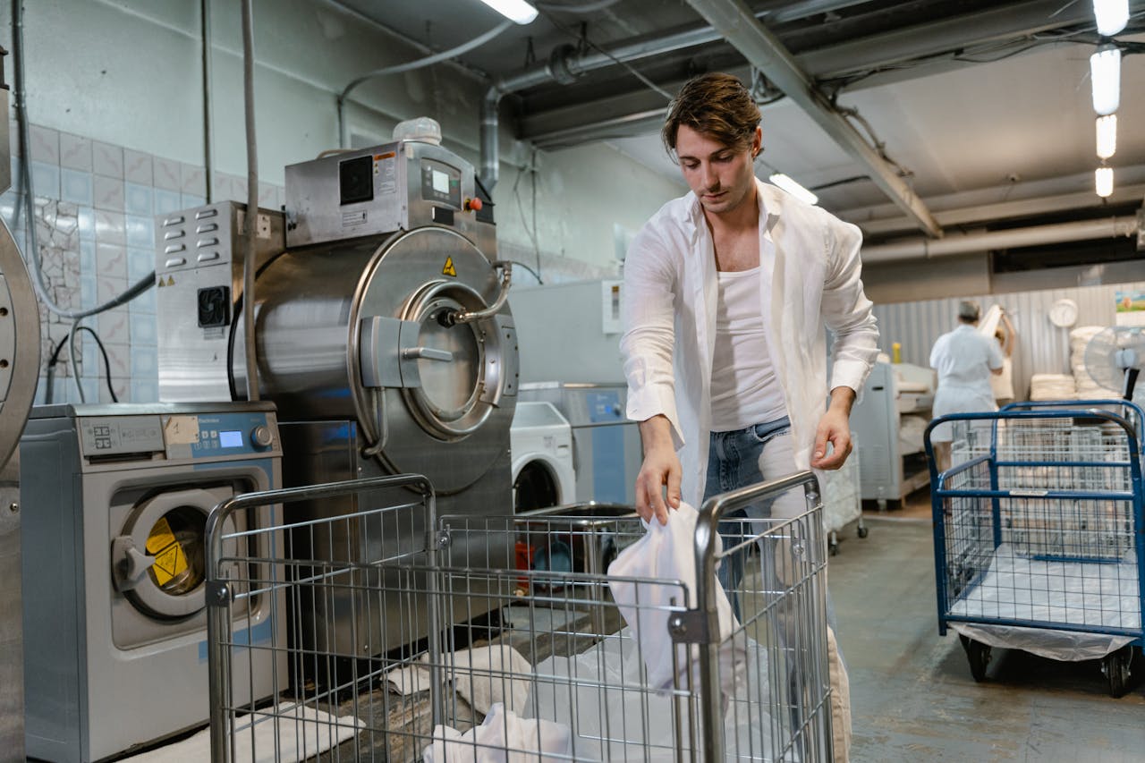 A man organizing laundry in an industrial facility with machines and carts.