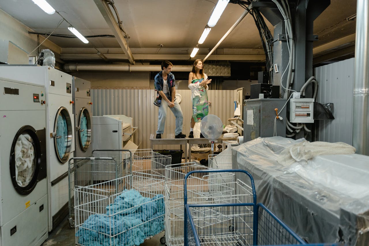 Two people take a break in a busy industrial laundry facility, surrounded by machines and laundry carts.